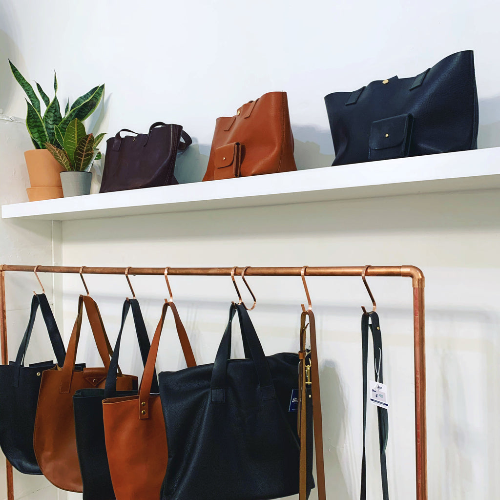 Totebags displayed on a shelf and black and brown bags hanging from a clothing rod